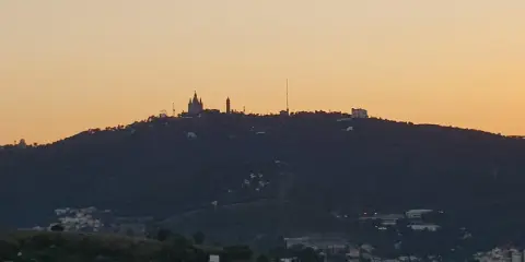 Silhouetten von Gebäuden auf einem bewaldeten barcelona berg im Abendlicht.