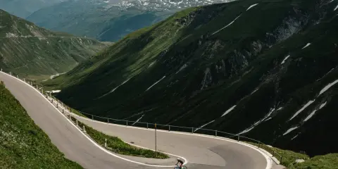 Radfahrer auf einem Transalp Rennrad meistert Serpentinen in den Alpen. Majestätische Bergkulisse mit Schneefeldern.
