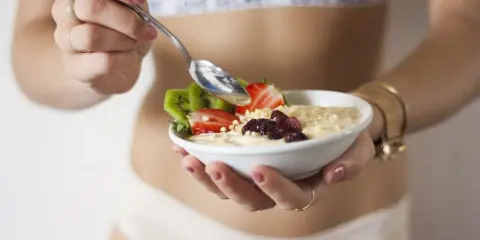 Mujer disfrutando un tazón de avena con fresas, kiwi y frutos secos. Un desayuno ideal para una dieta deficit calorico.
