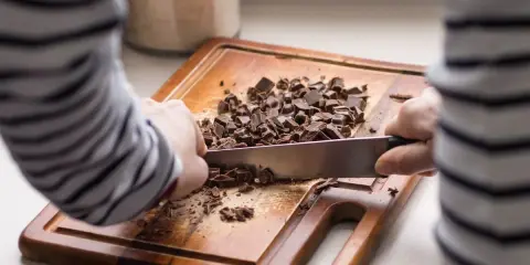 Une personne utilise un couteau pour comment casser une tablette de chocolat en pépites sur une planche à découper en bois.