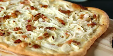 Flammekueche généreuse garnie d'oignons crus ou cuits et de lardons croustillants, prête à être dégustée.