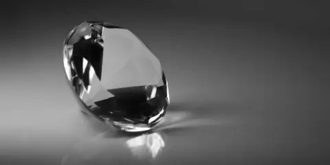 Un diamante sfaccettato riflette la luce su una superficie lucida. Il suo fascino misterioso evoca il significato dei diamanti neri: forza e resilienza.