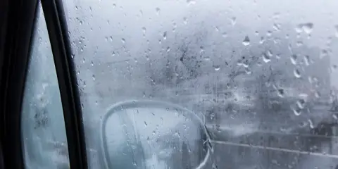 Gotas de lluvia en el cristal del coche, reflejando el exterior y el espejo retrovisor. Una escena que explica porque se empañan los cristales en días húmedos.