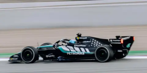 El Aston Martin AMR26 negro y turquesa acelera en la pista, con el logo de Petronas visible.