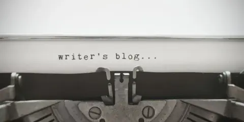 Maszyna do pisania z napisem "writer's blog..." na papierze. Idealny przykład wpisu na bloga po angielsku.