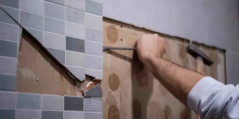 Persona usando una espátula para quitar azulejos de una pared.