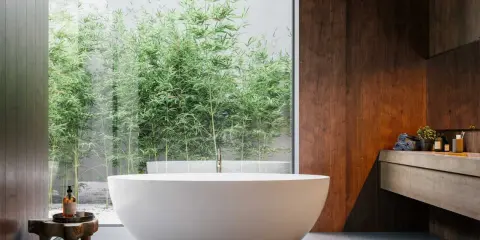 Mała łazienka w stylu spa z wolnostojącą wanną i widokiem na bambusowy ogród. Drewniane akcenty i kamienne płytki tworzą relaksującą atmosferę.