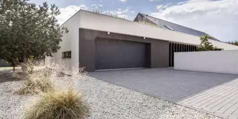 Moderne maison avec agrandissement garage, allée pavée, gravier blanc et végétation.