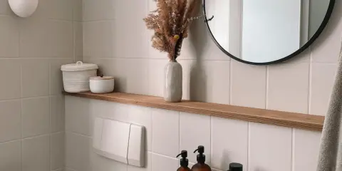 Étagère en bois dans une salle de bain carrelée, avec des décorations et un miroir rond.