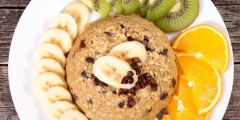 Un délicieux bowl cake flocon d'avoine garni de rondelles de banane, de tranches de kiwi et d'orange, parsemé de pépites de chocolat.