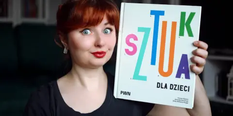 Kobieta z rudymi włosami trzyma książkę "Sztuka dla dzieci". Jej oczy są szeroko otwarte, a usta umalowane na czerwono.