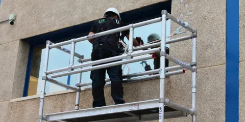 Trabajador en andamio modular, uno de los tipos de andamios, limpiando una ventana.