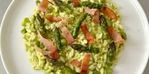 Risotto cremoso con asparagi freschi e croccanti strisce di speck, un piatto primaverile che delizia il palato.