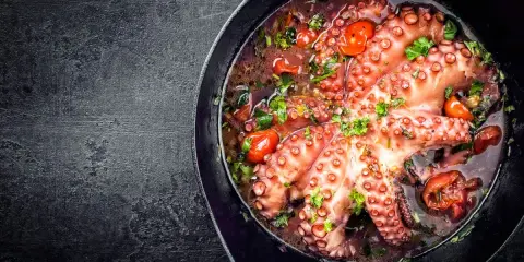 Polpo alla luciana in padella, con pomodorini e prezzemolo fresco. Un piatto succulento e profumato, pronto per essere gustato.