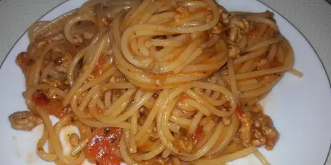Pyszne spaghetti bolognese z passaty, z mielonym mięsem i kawałkami pomidorów, podane na białym talerzu.