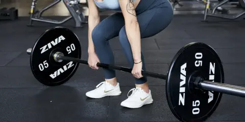 Donna in palestra si prepara per gli stacchi da terra con un bilanciere.