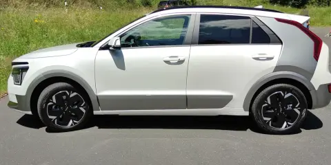 Biały Kia Niro EV z czarnymi felgami stoi na drodze, otoczony zielenią.