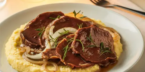 Fette di carne brasata su polenta cremosa, guarnite con cipolle caramellate e rosmarino. Un classico tra i piatti tipici veneti.