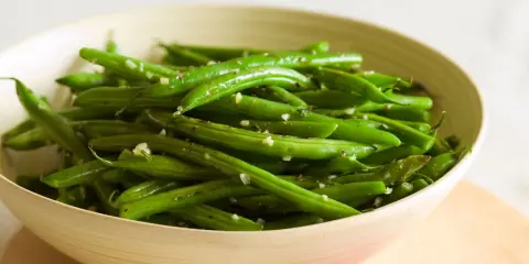 Fagiolini freschi saltati in padella con aglio e pepe, serviti in una ciotola di legno.
