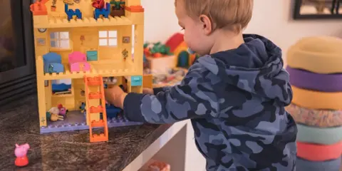 Kleiner Junge spielt mit einem Puppenhaus. Ein Schritt beim **Kinderzimmer ausmisten** ist, Spielzeug zu sortieren.