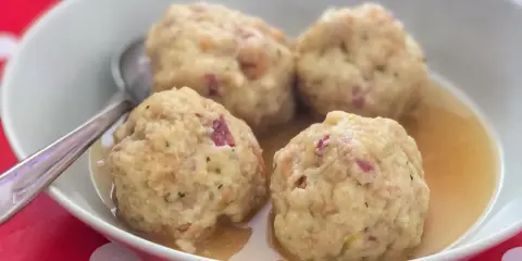Canederli in brodo, uno dei piatti tipici del Trentino Alto Adige, serviti in una ciotola bianca su un tovagliolo rosso a pois bianchi.