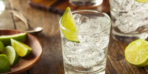 Erfrischender Gin Schnaps mit Eis und Limettenspalten auf rustikalem Holztisch.