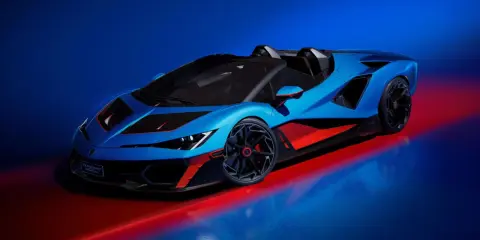 Ein blauer Lamborghini Veneno Roadster mit roten Akzenten steht auf einem glänzenden Boden, beleuchtet von rotem und blauem Licht.