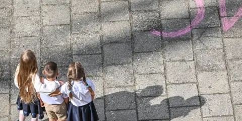 Trójka dzieci w szkolnych strojach patrzy na napis "szkoła społeczna co to" narysowany kredą.