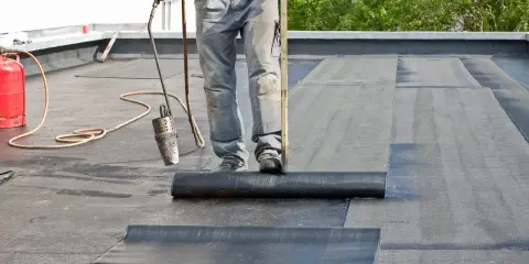 Dachdecker verlegt mit Brenner und Rolle Bitumenbahnen auf einem Flachdach.