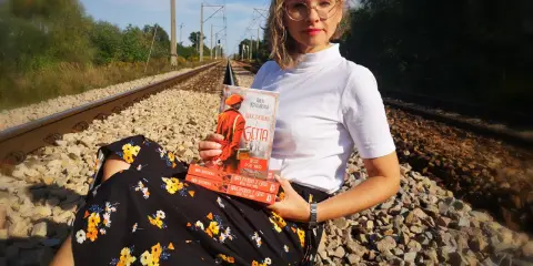 Kobieta z książką "Nauczycielka z Getta" siedzi na torach. Recenzja książki gwiazd naszych win po angielsku.