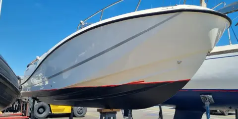 Le carénage d'un bateau blanc et gris, avec une ligne rouge sous la flottaison, est exposé au soleil.