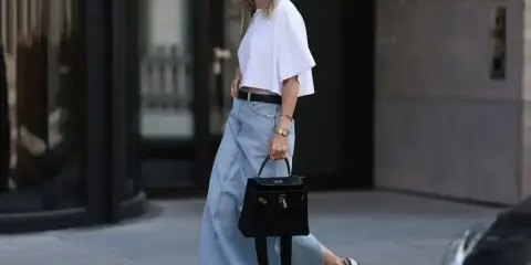 Kobieta w białej bluzce i długiej spódnicy jeansowej midi, z czarną torebką i sneakersami. Stylowe spódnica jeansowa midi stylizacje.