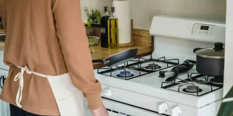 Un homme en tablier prépare à nettoyer graisse brûlée gazinière. Une poêle chauffe sur le feu.