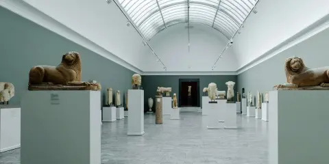 Starożytne rzeźby lwów i popiersi w muzeum w Kopenhadze, podświetlone przez świetlik w dachu.