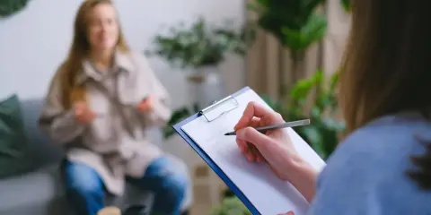Psychologia kliniczna w praktyce: terapeuta notuje objawy pacjentki, która opowiada o swoich problemach.
