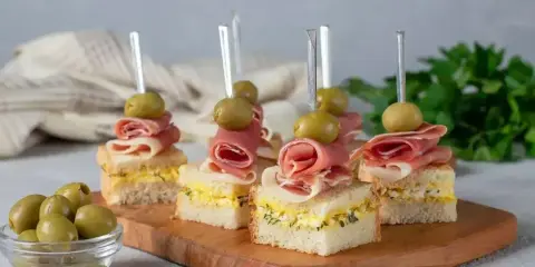 Eleganckie mini przekąski na imprezę: kanapki z szynką, jajkiem i oliwkami na wykałaczkach.