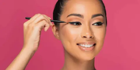 Une femme crée des "siren eyes" avec un eye-liner précis, son regard captivant promettant une beauté envoûtante.