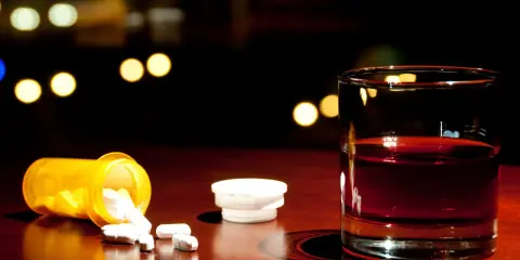 Szklanka z alkoholem i rozsypane tabletki paracetamolu na drewnianym blacie.