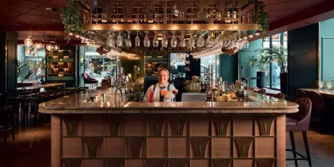 En glad bartender vid en elegant cocktail bar i Stockholm, med drinkar och glas på rad.