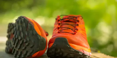 Leuchtend orange Trailrunning-Schuhe mit grobstolliger Sohle, bereit für neue Abenteuer. Perfekt, um bergschuhe neu besohlen zu lassen und wieder loszulegen.