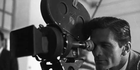 Pier Paolo Pasolini, con lo sguardo concentrato, osserva attraverso l'obiettivo di una cinepresa Arriflex, pronto a catturare la realtà.