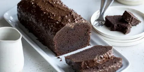 Un généreux gâteau au chocolat haut, nappé d'un glaçage croquant et parsemé de noisettes. Deux tranches sont déjà coupées, prêtes à être dégustées.