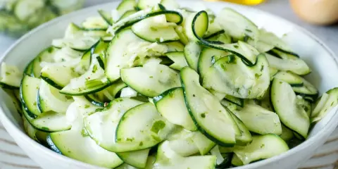 Frischer Salat aus dünn geschnittenen Zucchinischeiben, mariniert mit Kräutern und Öl. Perfekt, um Zucchini roh zu essen.
