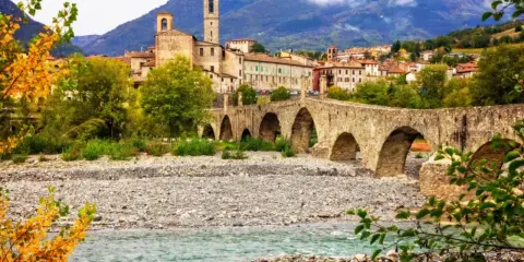 Ponte Gobbo a Bobbio, borgo dei borghi, con il fiume e le montagne sullo sfondo.