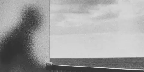 A silhouette of a person, reminiscent of a Peter Fetterman photograph, looks out at the ocean from behind a frosted glass.