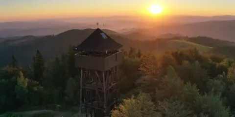 Wieża widokowa na Koziarzu o zachodzie słońca, otoczona lasem i górami.