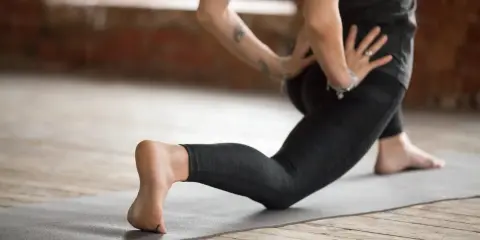 Kobieta ćwiczy jogę, pogłębiając skłon w wykroku, by rozciągnąć biodra i zniwelować tzw. hips dips.