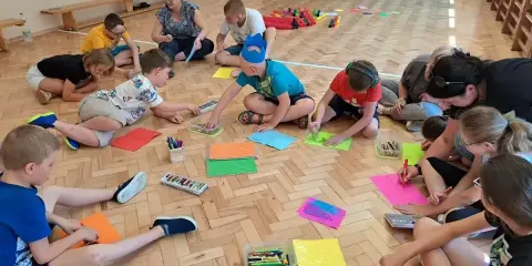 Dzieci biorą udział w zabawach animacyjnych, rysując na kolorowych kartkach.