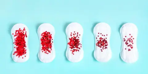 Pięć podpasek z czerwonymi cekinami, symbolizującymi lekkie krwawienia z pochwy, ułożonych w rzędzie na niebieskim tle.