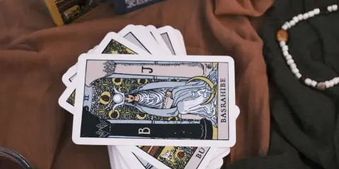 Karty tarota ułożone na brązowym materiale. Jedna karta, przedstawiająca postać z księżycem i owocami, jest na wierzchu. To idealny obrazek na **tarot na tydzień**.